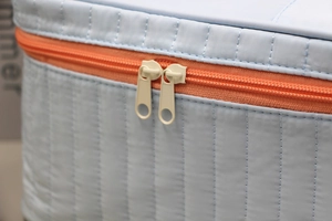 Close-up of quilted light blue makeup bag featuring orange zipper and yellow pulls