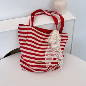 Close-up of red and white striped canvas tote bag with white lace ribbon and metal logo