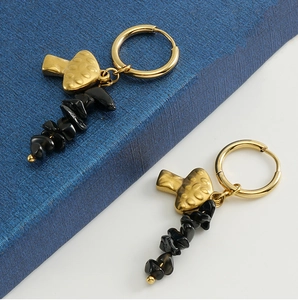 Detail of 18k gold mushroom earrings with black natural stone beads on a textured surface