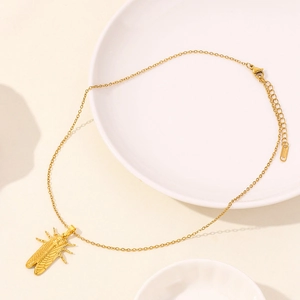 Detailed view of a golden cicada pendant necklace resting on white ceramic plates