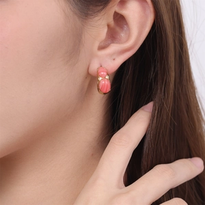 Detailed close-up of a model wearing gold C-shaped earrings with coral oval stone beads