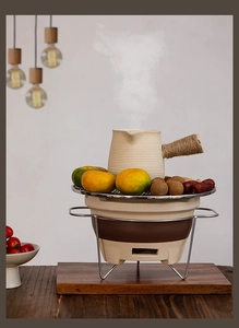Steaming ceramic teapot heating on a vintage charcoal stove with fruits on the grill