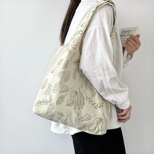 Detail of canvas tote bag with green leaf patterns worn by a model in casual style