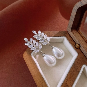 Macro view of leaf-shaped rhinestone earrings with teardrop pearls on a wooden box