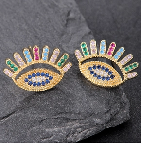 Macro detail of gold evil eye stud earrings with colorful zircons on a dark stone
