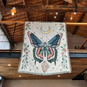 Close-up of bohemian woven throw blanket with butterfly and moon patterns on a wood rail