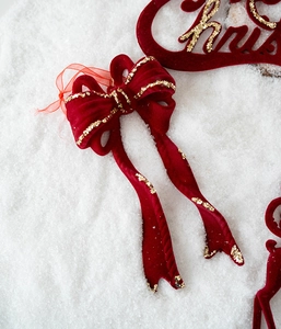 Détail d'un nœud de Noël en velours rouge avec paillettes dorées sur fond de neige