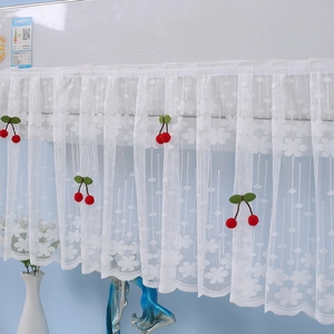 Detail of white lace cabinet curtain with floral pattern and red cherry ornaments