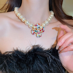 Close-up of pearl necklace with colorful gemstone cross pendant on model with black feathers