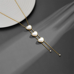 Golden heart pearl necklace with tassel detail on a textured dark background