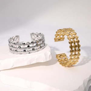 Minimalist geometric gold and silver plated woven open bangle on a stone pedestal