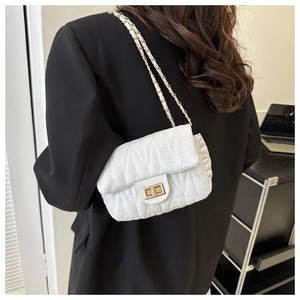 Close-up of white quilted leather crossbody bag with chain strap on a black blazer