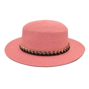 Détail d'un chapeau de paille rose avec chaîne dorée élégante et ruban noir décoratif