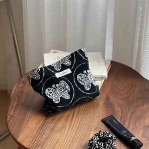 Detail of black cotton canvas cosmetic bag with white butterfly embroidery and label