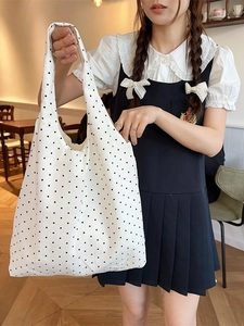Minimalist white canvas tote bag with black polka dots shown in a lifestyle cafe setting