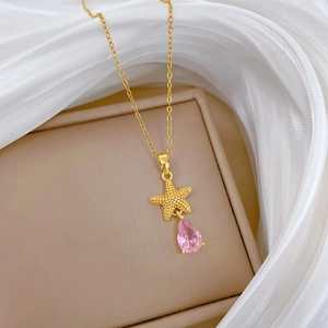 Detail of gold starfish necklace with pink teardrop crystal on beige box and silk