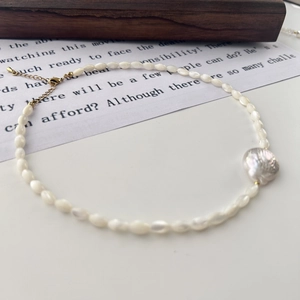 Detail of baroque pearl necklace with golden clasp and small rice pearls on wood