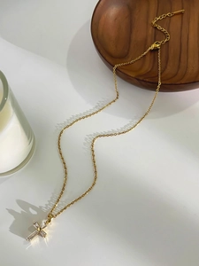 Close-up of a gold cross necklace with baguette-cut zircons on a dark wood tray