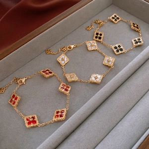 Three 14K gold plated clover bracelets with red, white, and black enamel inlays on a grey tray