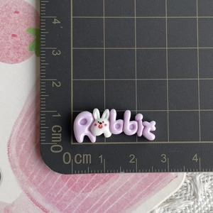 Close-up of a 3cm purple resin rabbit letter charm on a black measuring cutting mat