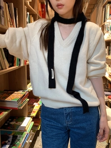 Detail shot of black slim plush scarf with 'nice moment' tag worn over a white V-neck sweater