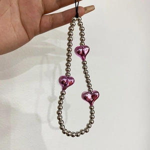 Handheld silver beaded phone strap featuring three metallic pink heart charms on white wall