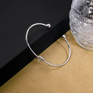 Detail of silver knot cuff bracelet with polished finish on a textured background