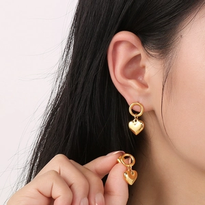 Close-up of a model wearing a gold heart pendant earring with a polished metal finish