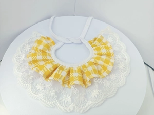 Close-up of yellow plaid pet bib with delicate white lace edge and adjustable tie strings