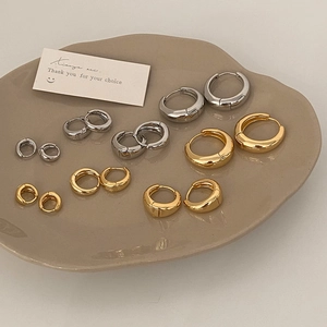 Various sizes of minimalist gold and silver hoop earrings on a ceramic display tray