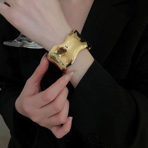 Macro shot of a high-polish irregular wave-edged wide bangle in a mirror gold finish