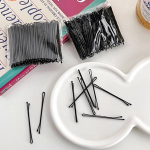 Flat lay of bulk black metal bobby pins in plastic bags on a styled aesthetic desk
