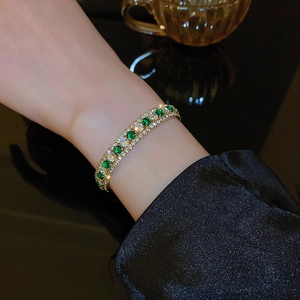Close-up of luxury gold bracelet featuring emerald green gems and zircon pavé detailing