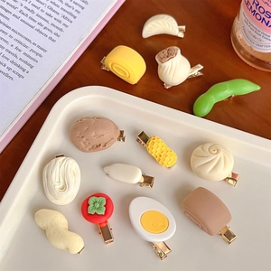 Variety of realistic food-shaped hair clips including dumplings and eggs on a white tray