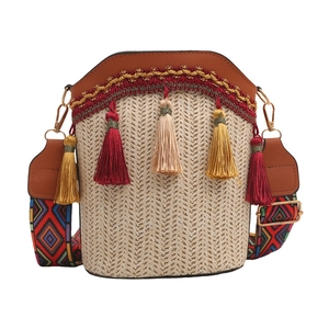 Detail of woven straw bucket bag featuring brown leather trim and colorful ethnic strap