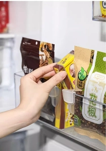 Transparent clip-on refrigerator organizer bin holding various spice packets and bags