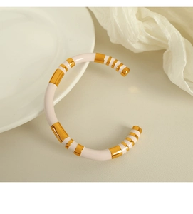 Detail of a white enamel cuff bangle with golden stripe patterns on textured fabric