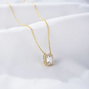 Macro shot of gold square zircon necklace with emerald-cut stone on white silk
