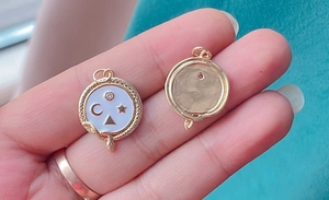 Detail view of a gold round pendant with white enamel and star moon charms on hand