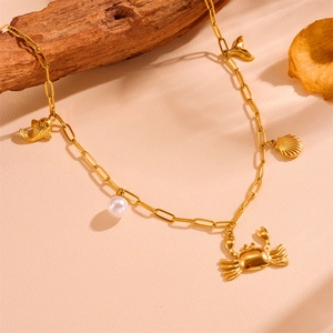 Détail du collier chaîne trombone dorée avec pendentifs crabe, perle blanche et coquillage
