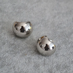 Macro detail of teardrop-shaped silver earrings on grey plush fabric background