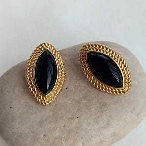 Detail of vintage gold textured earrings with black oval stones on a grey pebble