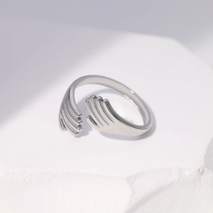 Detail of silver hugging hands ring on a white marble stone with elegant shadows