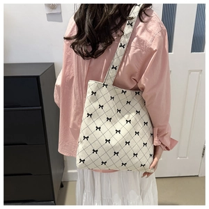 Dettaglio della borsa tote in velluto crema con motivi a fiocco nero su una modella