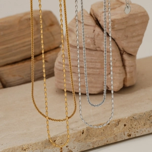 Colliers minimalistes en or et argent sur pierre naturelle beige au style industriel