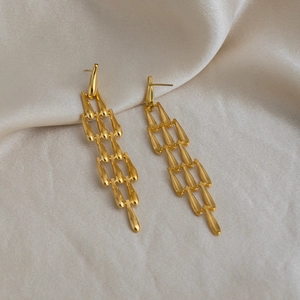 Détail de boucles d'oreilles pendantes dorées sur un fond de tissu en soie crème
