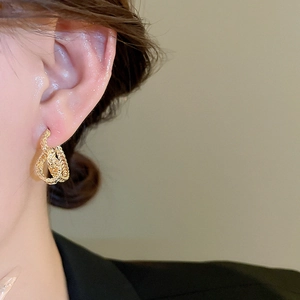 Close-up of golden twisted knot geometric C-shaped stud earrings worn by a model