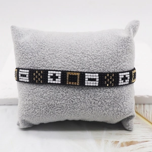 Minimalist gold and black geometric Miyuki beaded bracelet with a cross pattern on a pillow