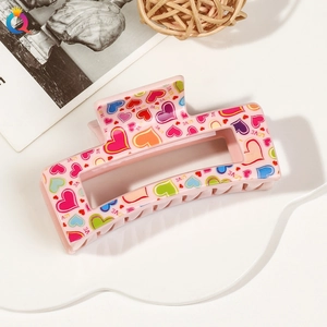 Close-up of pink plastic hair claw clip with colorful heart patterns and LOVE text