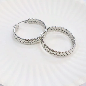 Close-up of silver geometric hoop earrings with detailed wheat ear texture